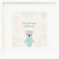 An inspirational print with a graphic of Claire the koala in mint on a blush-colored background decorated with leaves and the words “Daydream believer” in mint.