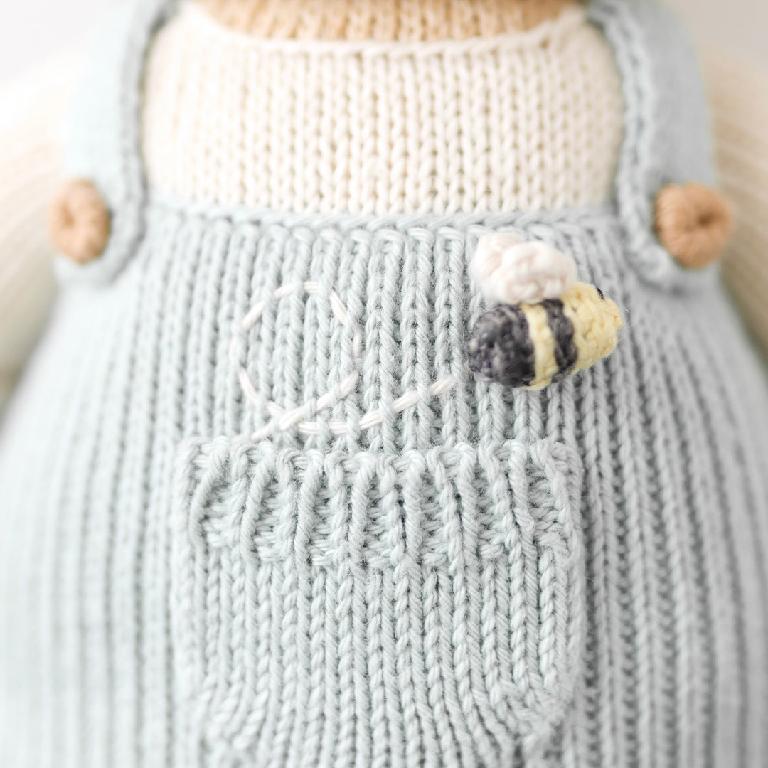 A close-up showing the hand-knit details of the little bee stitched above Charlie’s pocket.