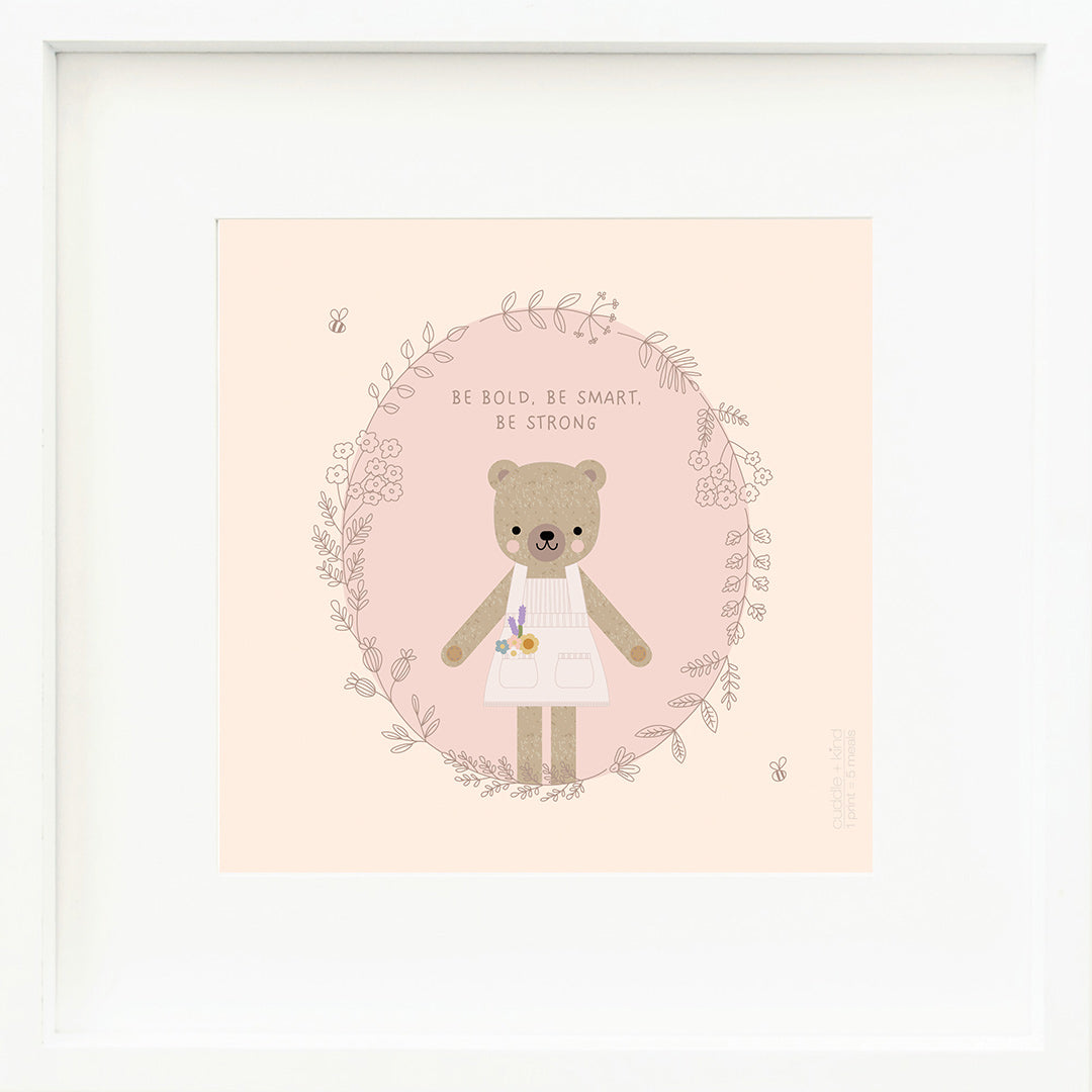 An inspirational print with a graphic of Goldie the honey bear in a circle of floral and leafy vines with a pair of bumblebees. The background is purple and pink and above Goldie’s head are the words “Be bold, be smart, be strong”