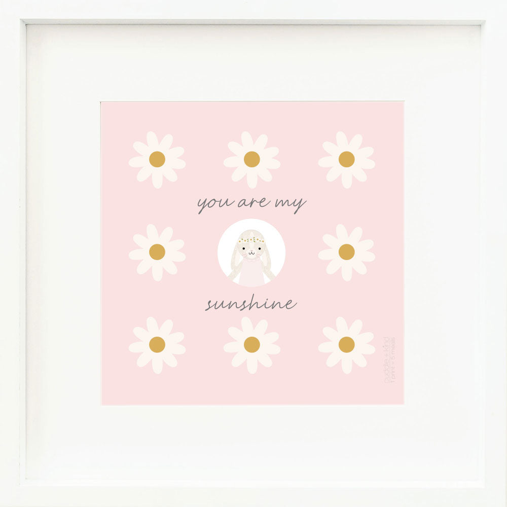 An inspirational print with a graphic of Hannah the bunny in blush, on a pink background decorated with daisies and the words “You are my sunshine” in dark gray.