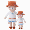 Chelsea the cat in the regular and little sizes, shown from the front. Chelsea is wearing a white dress with blue embroidered details, a brown hat and brown boots.