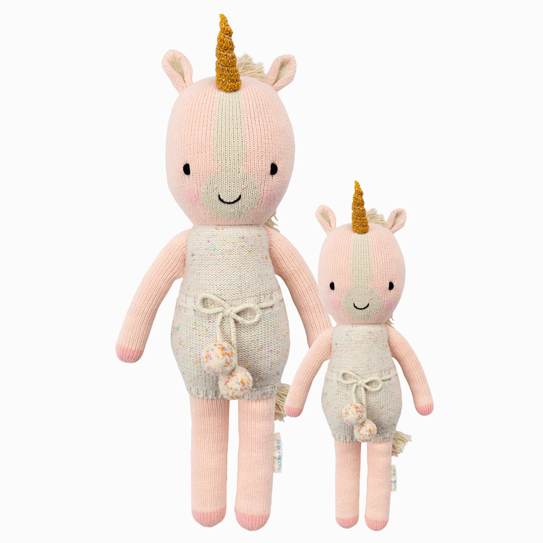 Ella the unicorn in the regular and little sizes, shown from the front. Ella is wearing a white romper with confetti polka dots and a pom-pom tie.