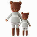 Oliver the bear in the regular and little sizes, shown from the front. Oliver has gray shorts and a sweater that says “Kind.”