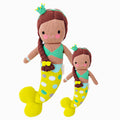 Pearl the mermaid in the regular and little sizes, shown from the front. Pearl has brown hair that’s braided with a yellow bow. She’s wearing a green knitted crown, and her tail is yellow with gray, white, green and blue polka dots.
