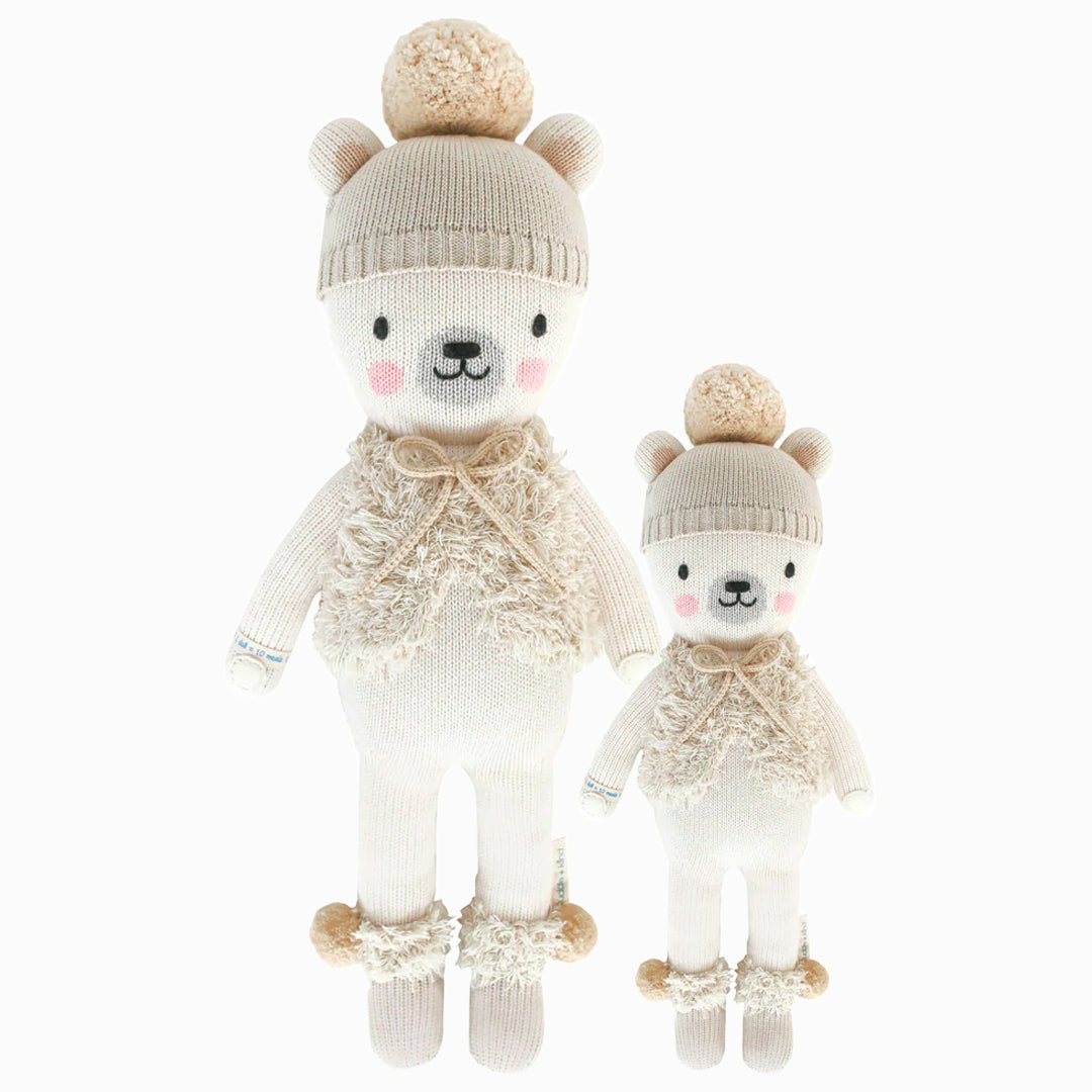 Stella the polar bear in the regular and little sizes, shown from the front. Stella has a cream-colored pom-pom hat, a fluffy vest with a bow, and pom-poms on her boots.