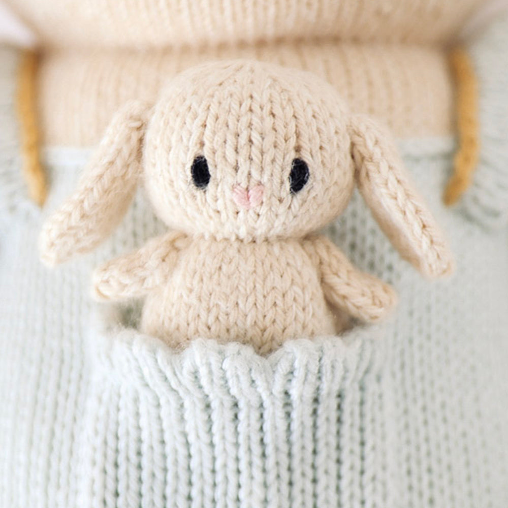 A close up of the tiny hand-knit bunny attached in Briar the bunny’s pocket. The tiny bunny has a teeny pink, heart-shaped nose.