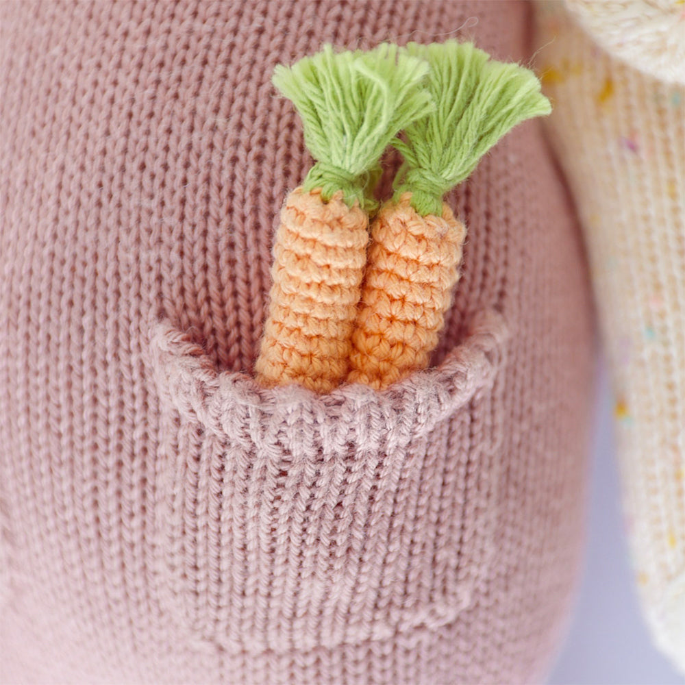 A close-up showing two hand-knitted carrots in the pocket of Harper’s jumper.