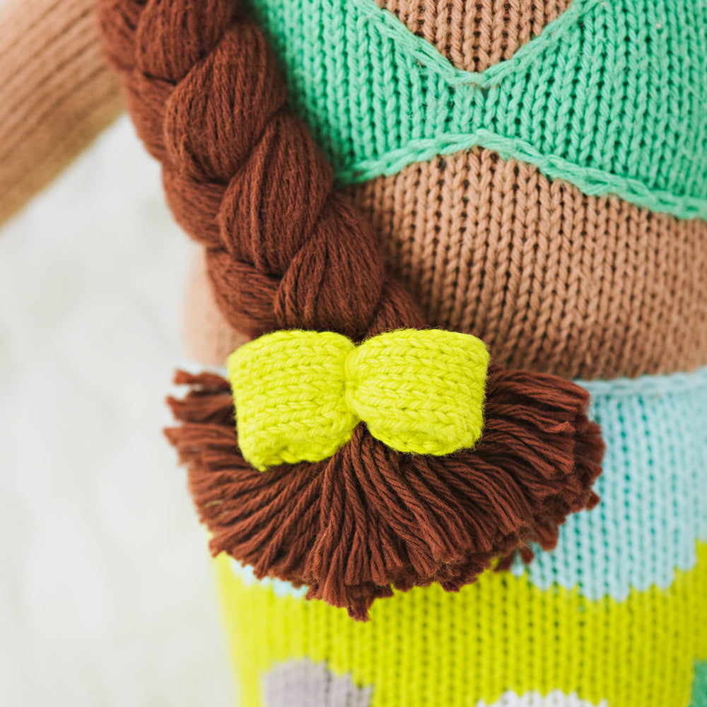 A close-up showing the hand-knit details on Pearl, including a yellow bow on her yarn braid.