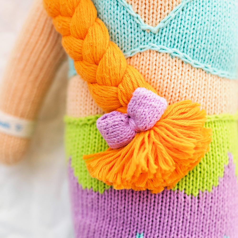 A close-up showing the hand-knit details on Isla, including a purple bow on her yarn braid.