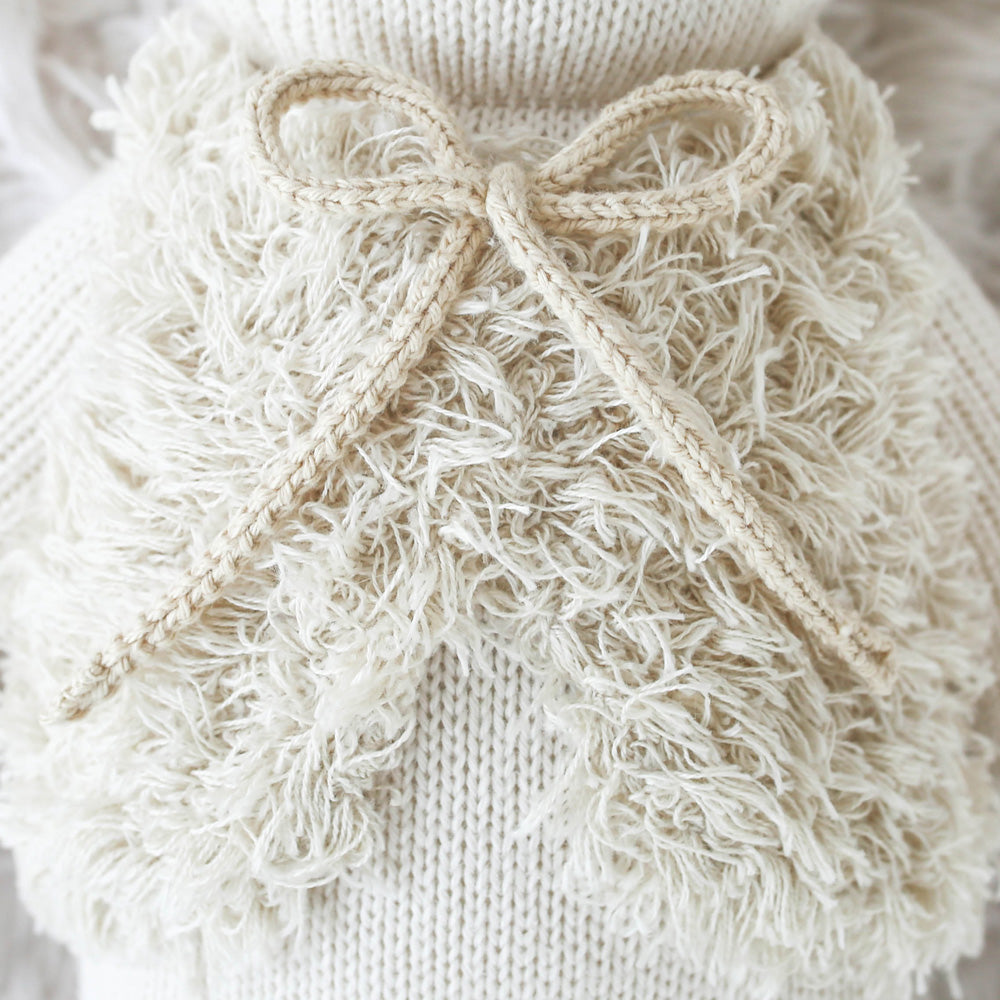 A close-up showing the hand-knit details on Stella’s fluffy vest and yarn bow.