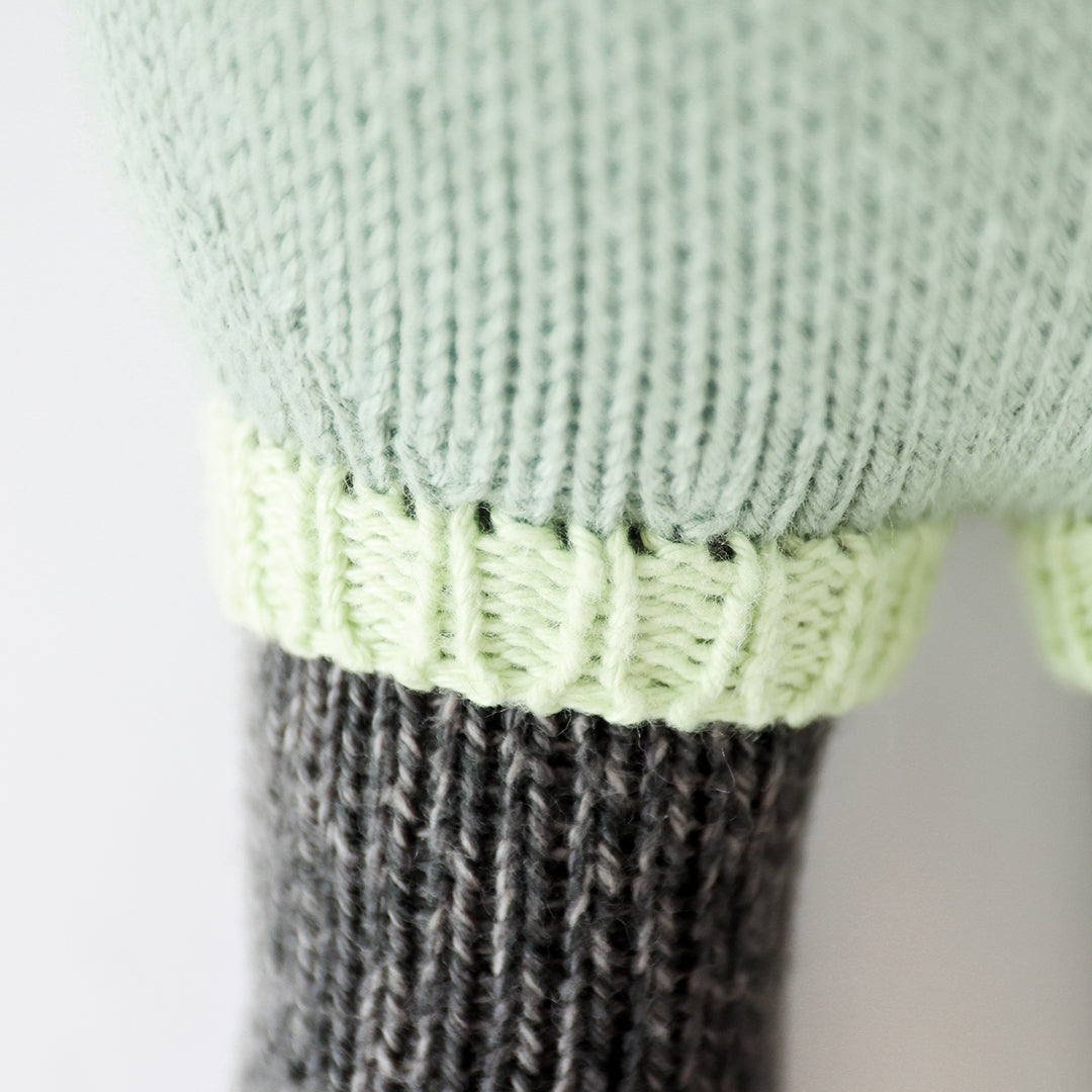 A close-up showing the hand-knit details of the chartreuse ribbed cuffs on Paxton the panda’s romper.