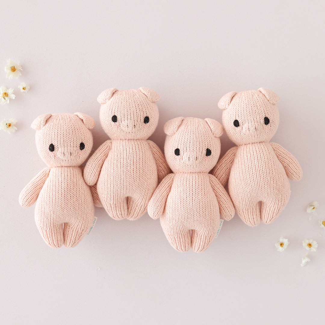 A group of four baby piglet stuffed dolls with tiny daisies in the background.