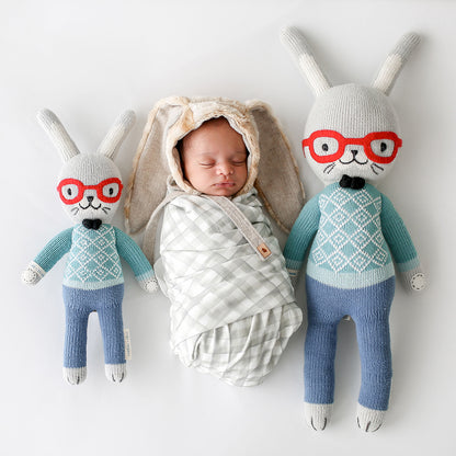 A sleeping baby in a bunny hood lying side-by-side with two Benedict the bunny dolls in the regular and little sizes.