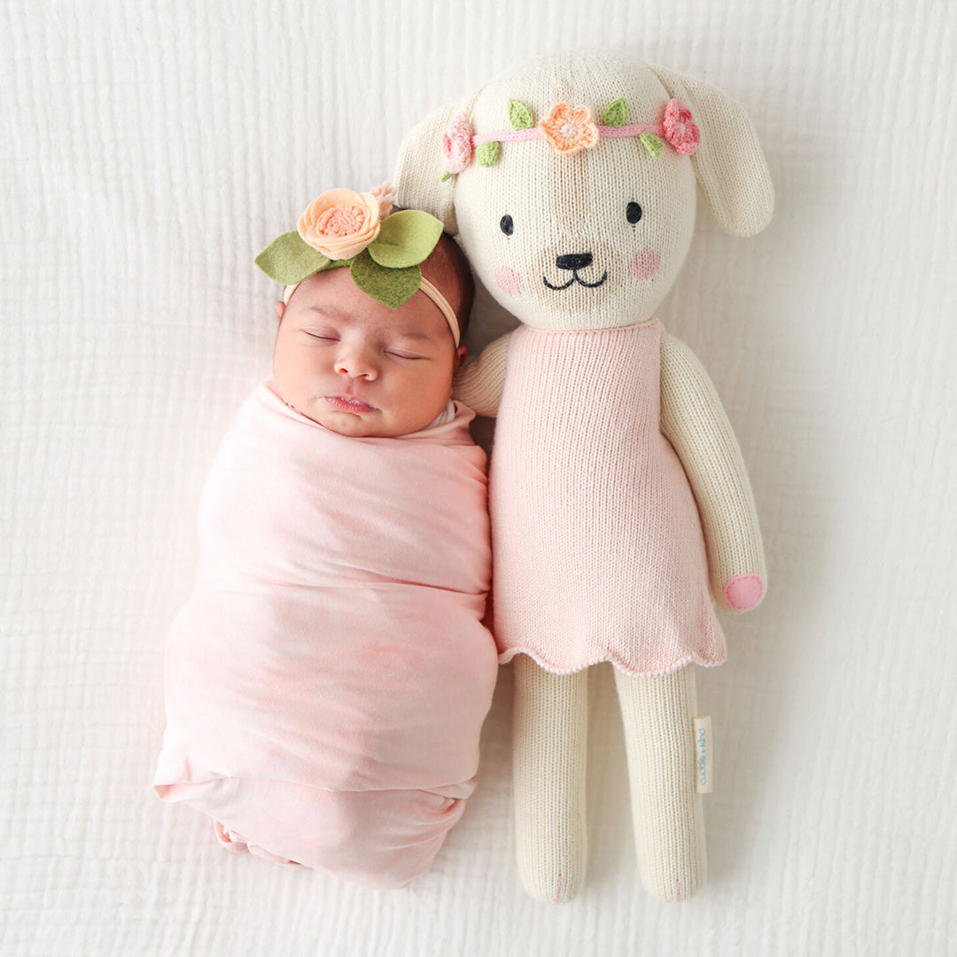 A sleeping baby lying snuggled beside Charlotte the dog. The baby is wearing a floral headband similar to Charlotte the dog’s.