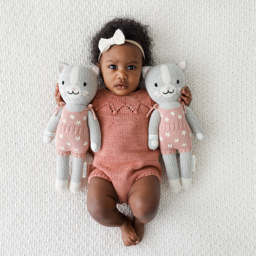 A baby holding two Daisy the kitten dolls.