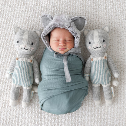 A sleeping baby in a cat hood lying in between two Dylan the kitten dolls.