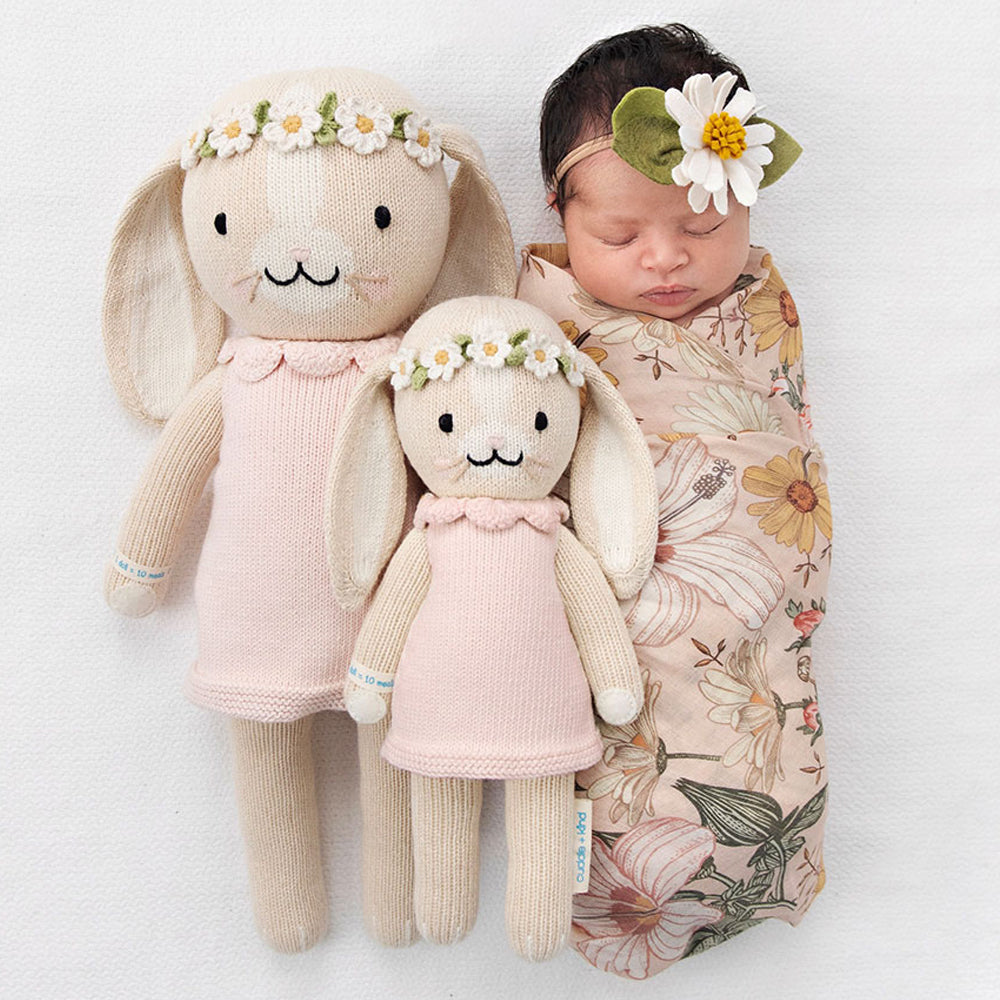 A sleeping baby, wearing a daisy headband, with two Hannah the bunny dolls in the regular and little sizes.