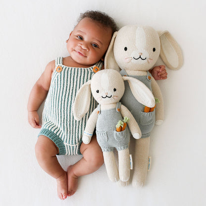 A baby snuggled beside two Henry the bunny dolls in the little and regular sizes.