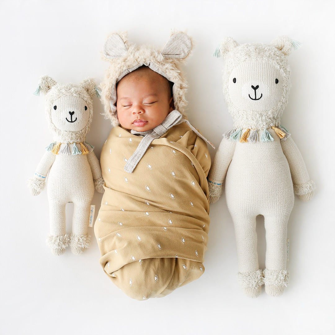 A sleeping baby snuggled between two Lucas the llama stuffed dolls in the little and regular sizes.