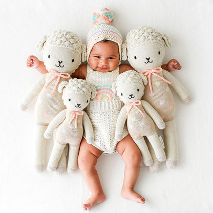 A smiling baby with their arms around four Lucy the lamb dolls in the regular and little sizes.