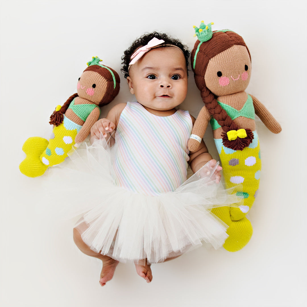 A baby with two Pearl the mermaid dolls in the little and regular sizes.