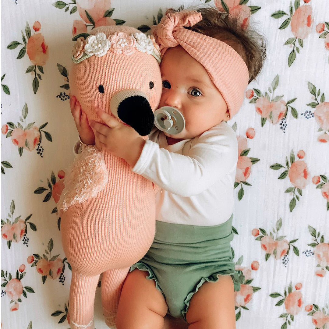 A baby in a soft, pink headband snuggling with Penelope the flamingo.