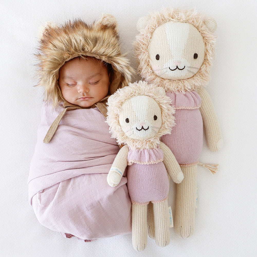 A sleeping baby in a fluffy lion hood with Savannah the lion dolls in the little and regular sizes.