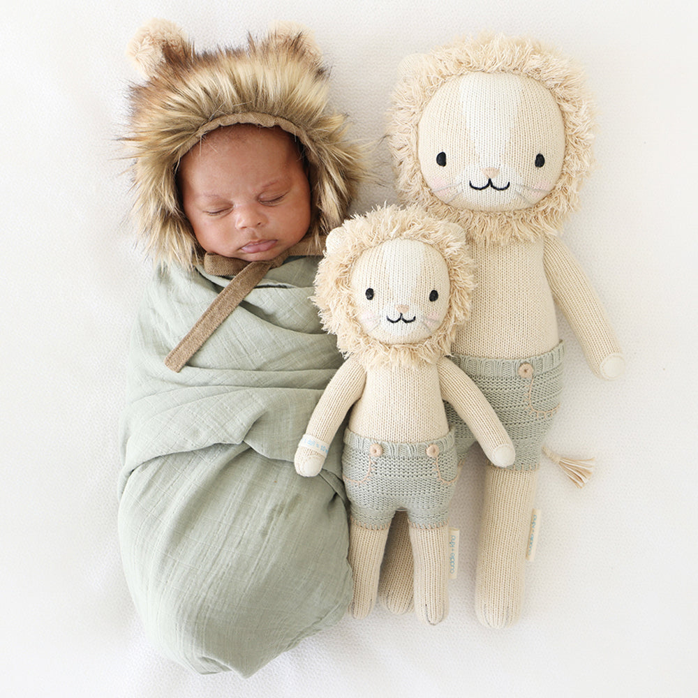 A sleeping baby in a fluffy lion hood with Sawyer the lion dolls in the little and regular sizes.