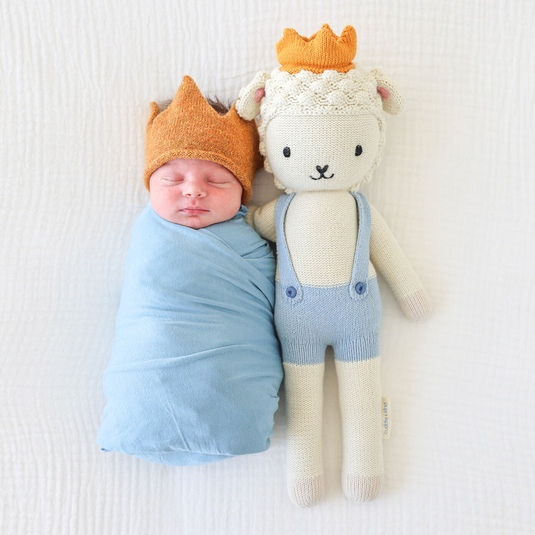 A sleeping baby with a Sebastian the lamb doll in the regular size. The baby has a knitted crown to match Sebastian.