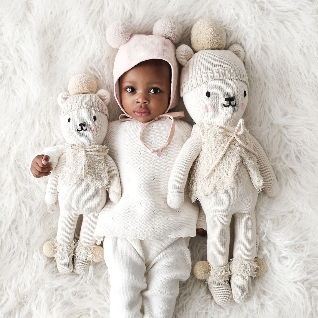 A baby in a pom-pom hat with two Stella the polar bear dolls in the little and regular sizes.