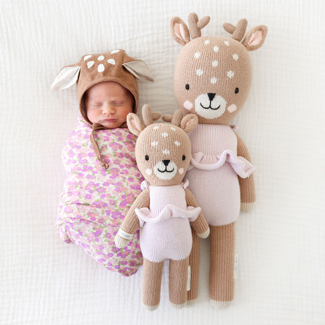 A swaddled baby wearing a deer hood snuggled beside two Violet the fawn, in the regular and little sizes.