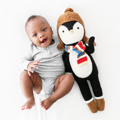 A laughing baby with his arm around an Everest the penguin stuffed doll.