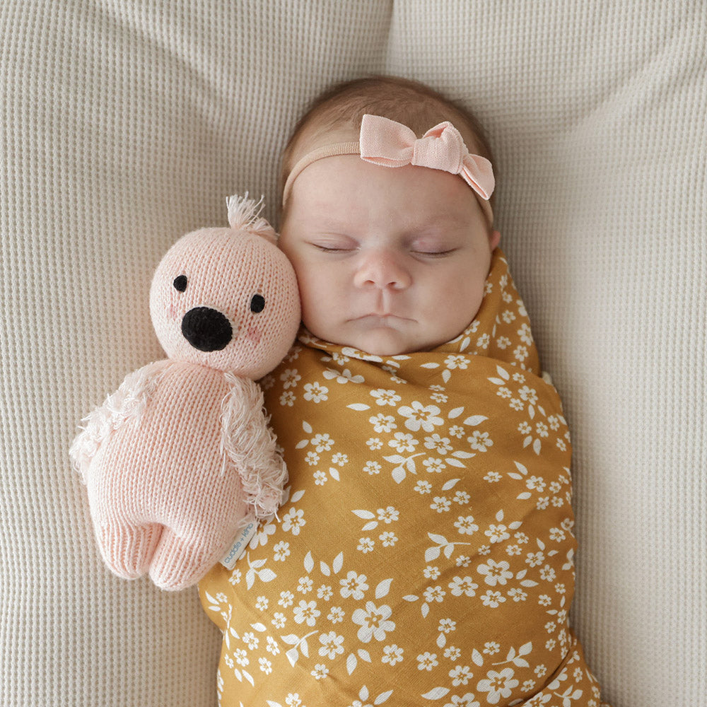 A sleeping baby snuggled next to a baby flamingo doll.