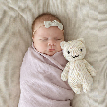 A sleeping baby snuggled next to a baby kitten doll.