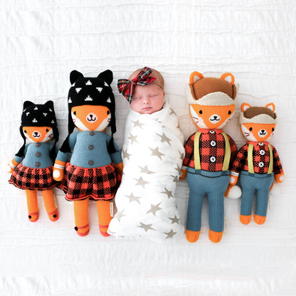 A sleeping baby wearing a plaid bow, lying between four hand-knit stuffed animals: Sadie the fox and Wyatt the fox in the little and regular sizes.