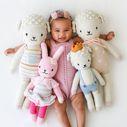 A smiling baby snuggled up with four cuddle and kind stuffed dolls.