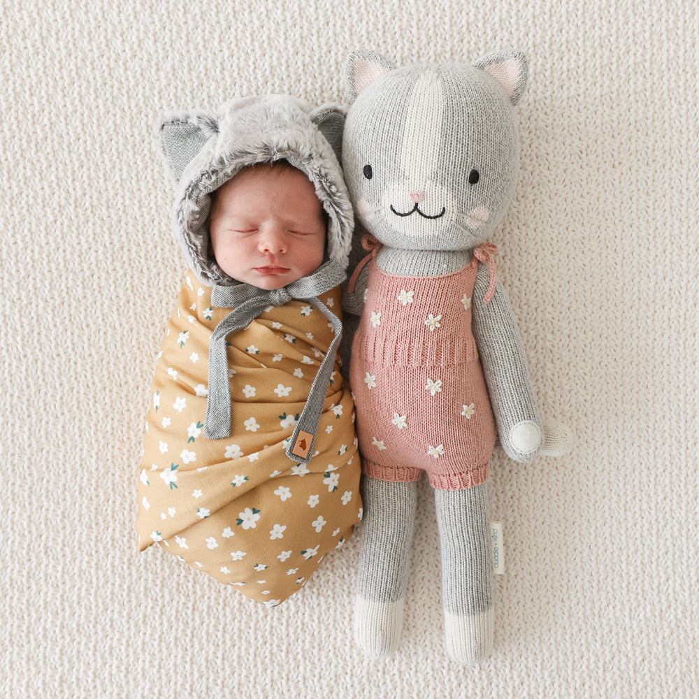 A sleeping baby in a cat hood with a Daisy the kitten stuffed doll.