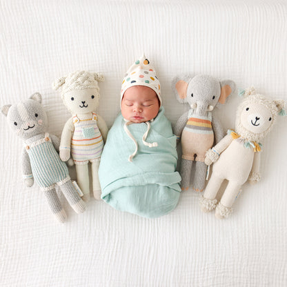 A sleeping baby wrapped snugly in a blanket, nestled between four hand-knit dolls.