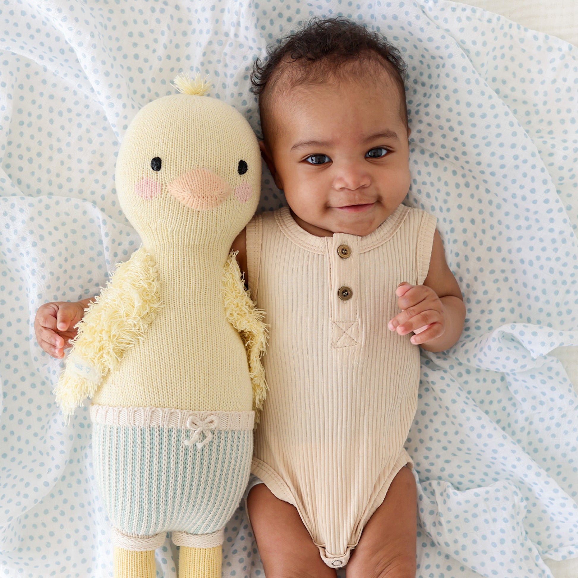 A smiling baby with their arm around Finley the duckling.