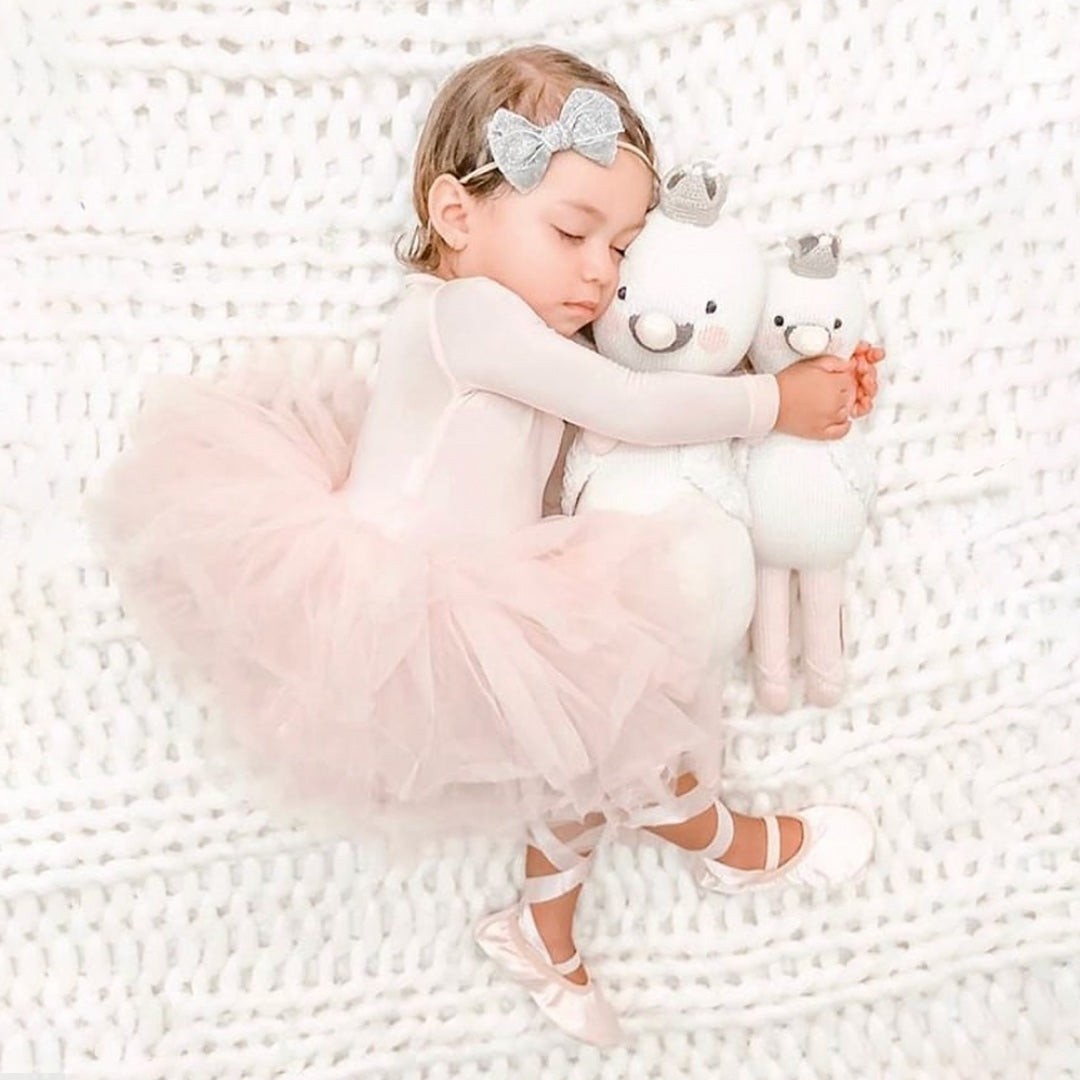 A sleeping baby, in ballet slippers and a tutu, with their arms around two Harlow the swan, in the regular and little sizes.