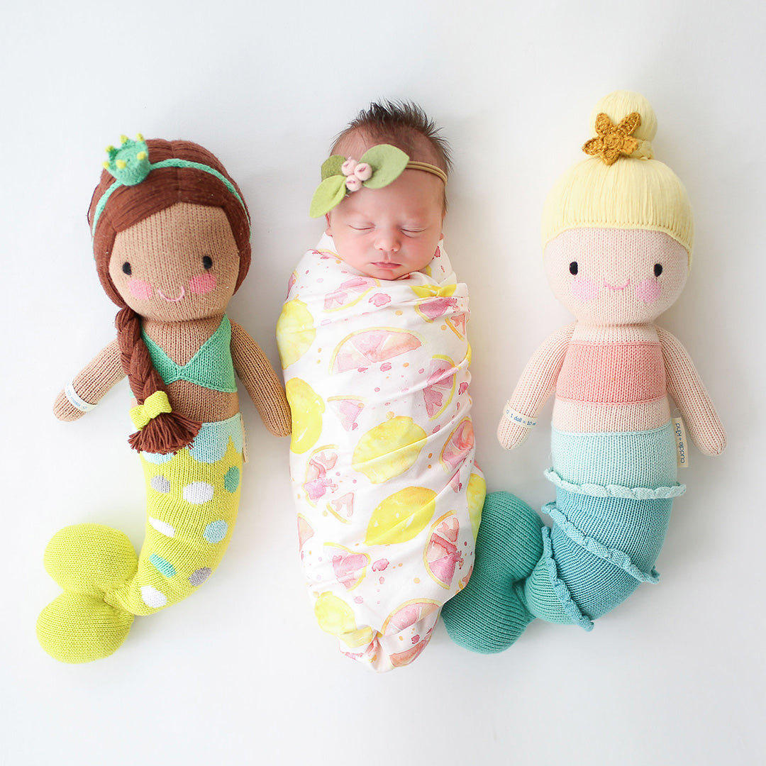 A sleeping baby with two mermaid stuffed dolls: Pearl and Skye.