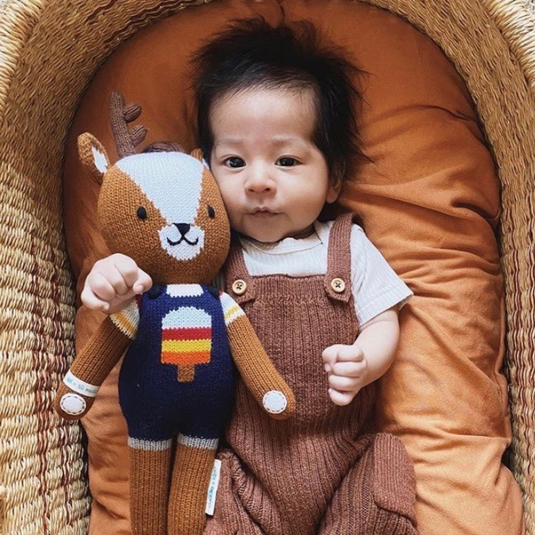 A sleeping baby in a fluffy deer hood, nestled between Scout and Willow the deer stuffed dolls.