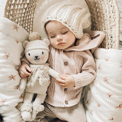 A sleeping baby in a knit hat snuggling a Stella the polar bear stuffed doll.