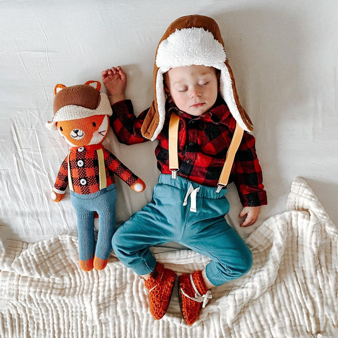 A sleeping baby with Wyatt the fox. The baby is wearing a brown winter hat, plaid shirt and suspenders to match Wyatt.