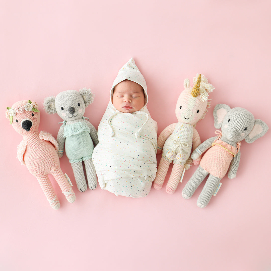 A sleeping baby lying between four cuddle and kind hand-knit dolls.