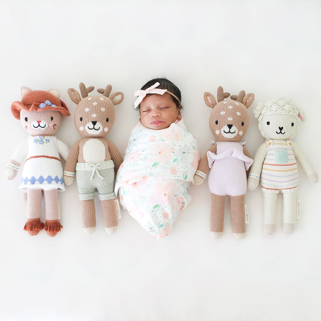 A sleeping baby lying in the middle of four cuddle and kind stuffed dolls.