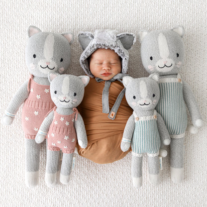 A sleeping baby in a cat hood with four knitted stuffed animals, Daisy the kitten and Dylan the kitten.