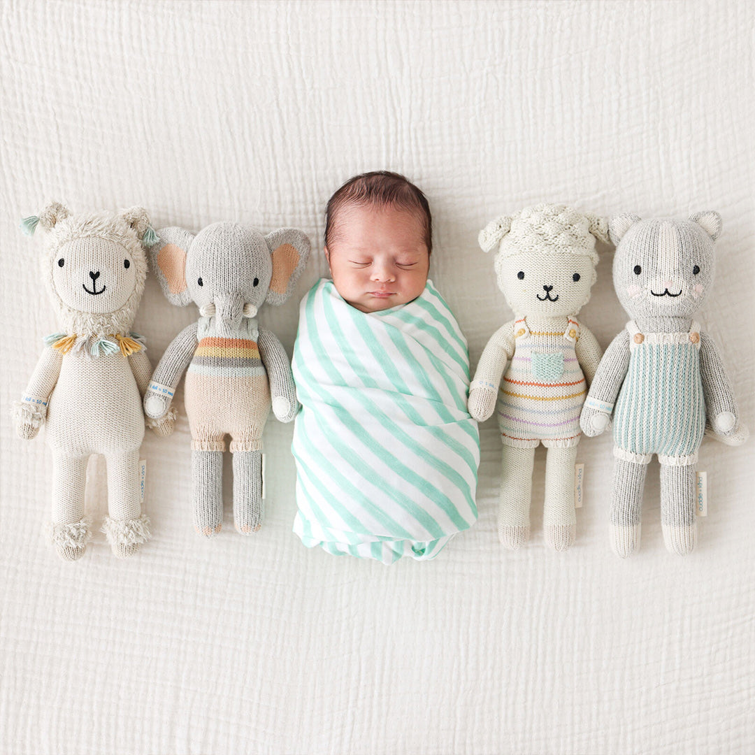 A sleeping baby surrounded by four hand-knit dolls: Lucas the llama, Evan the elephant, Avery the lamb and Dylan the kitten.