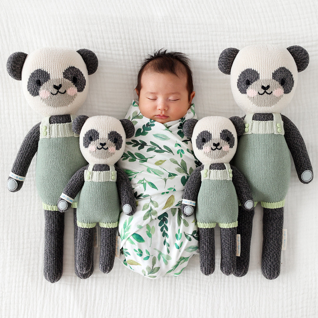 A swaddled, sleeping baby, lying in the middle of four Paxton the panda stuffed dolls.