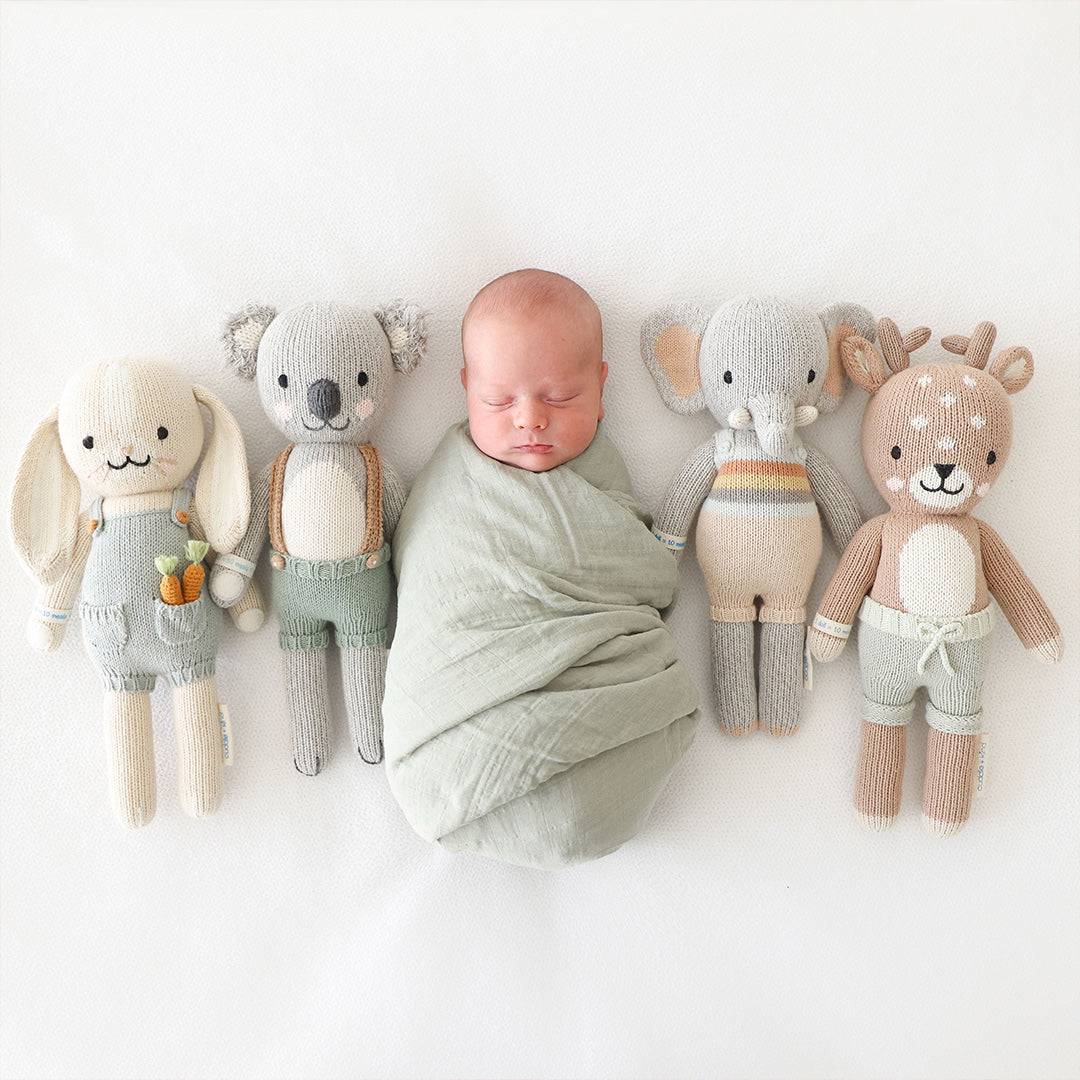 A sleeping baby in the middle of four cuddle+kind stuffed dolls: Henry, Quinn, Evan and Elliot.